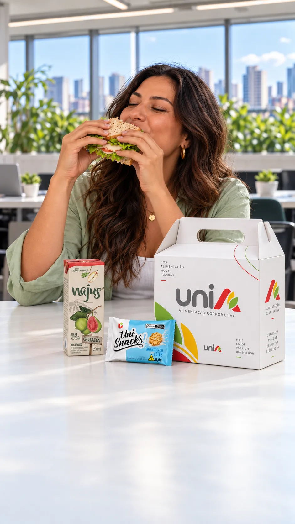Mulher saboreando sanduíche no escritório com kit lanche UniA, Uni Snacks e suco Najus de goiaba